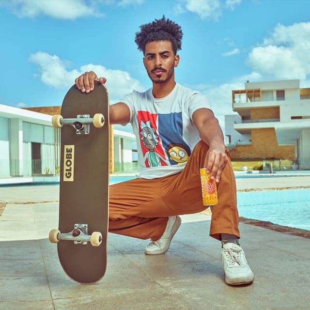 A boy with a skateboard  in one hand and a can in other 